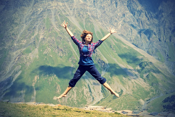 Young woman jumping with hands up against the mountain