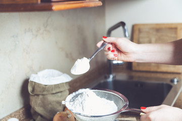 Female hand holding spoon and sieve flour