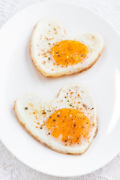 Fried eggs in the form of heart on white plate, vertical