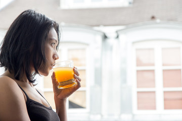 Young woman standing at an open window and drinks orange juice