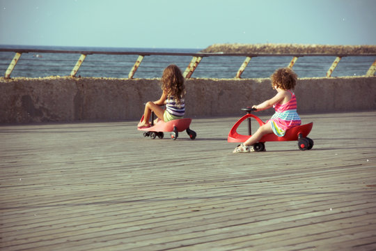 Two little girls riding on toy car (Swing Car \ Bimba) on the jetty by the sea
