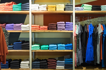 Various color sweatshirts at shelf and shirts on hangers in shop, Italy - 98225555