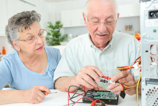 Elderly man checking computer with multimeter