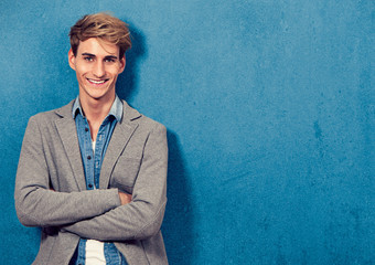 smiling young man leaning beside a blue wall