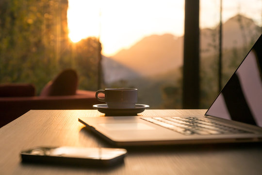 Computer Coffee Mug and Telephone on black wood table sun rising