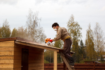 man paints wooden shelter with spray gun - Powered by Adobe