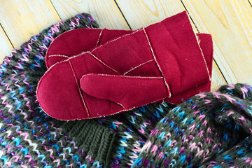 close up of knitted hat, scarf and mittens gloves in grey ,bordeaux wine red blue and purple colors on a wooden shelves planks table with a empty room copy space
