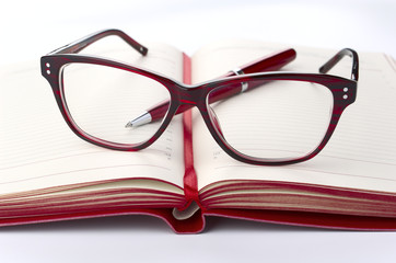 Red Daily planner with eyeglasses and pen, closeup