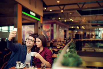 Happy young couple taking selfie with smart phone at cafe in mall. Copy space for your text. Shallow depth of field. Very useful photo for processing with one click on edit image.