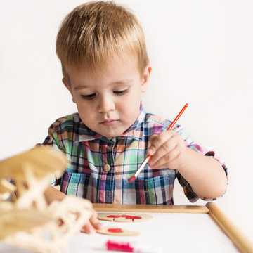 Adorable kid playing on his table with watercolors, painting a wooden parts of his airplane wooden toy. He is young designer with many ideas waiting to be found. Shallow depth of field.