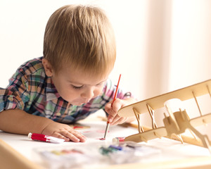 Adorable kid playing on his table with watercolors, painting a wooden parts of his airplane wooden...
