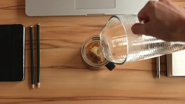 Tee wird in einer Glastasse am Schreibtisch/Arbeitsplatz aufgegossen
