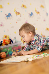 Adorable kid playing in a room with his toys. He is young designer with many ideas waiting to be found. Very shallow depth of field.