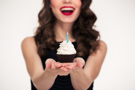 Cheerful Beautiful Curly Young Woman Giving Birthday Cupcake With Candle