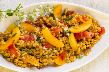 Bulgursalat mit Aprikosen und Tomaten in  weißer Schale mit frischen Kräutern dekoriert