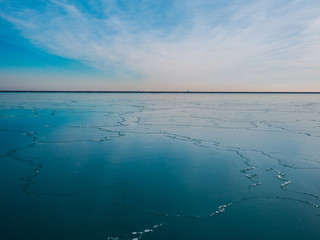 Color photograph of a frozen lake with cracks leading up to the horizon