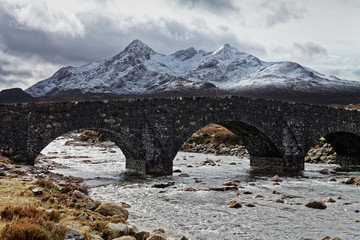 Old stone bridge over a wide stream in mountains