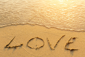 Inscription LOVE on sea beach sand, is soft the wave.