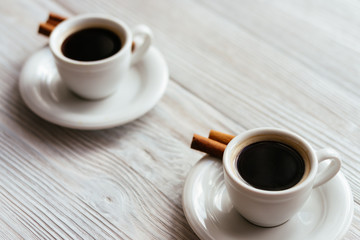 Two cups of espresso with cinnamon sticks on a white wooden tabl