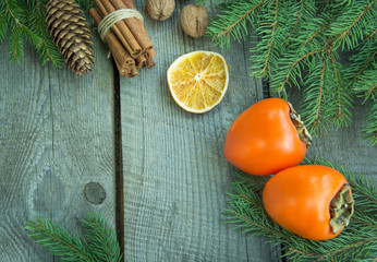 Christmas still life with fresh persimmon and cinnamon with pine tree on wooden background. Top view.