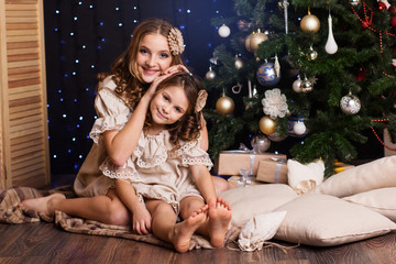 Two girls are sitting near christmas tree at home