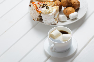 coffee with marshmallow and cake on white wooden background
