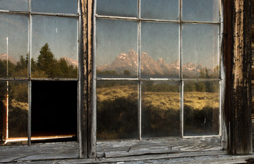the teton mountains reflected in old historic window panes and old frame.