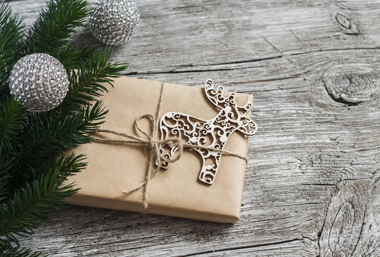 Homemade Christmas gift in kraft paper, wooden Christmas deer ornament, Christmas tree branches on rustic light wooden surface. Free space for text. Christmas wooden texture