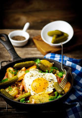 country breakfast from potatoes, with bacon and fried eggs in a pig-iron frying pan. style rustic. selective focus