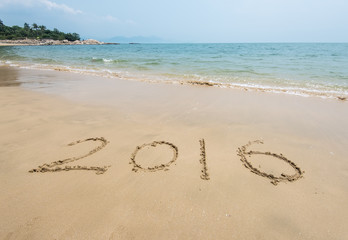 Year 2016 hand written on the white sand in front of the sea