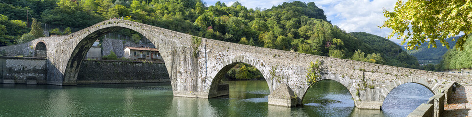 Fototapeta na wymiar panoramic view to old bridge with arch's through the green river in Italy