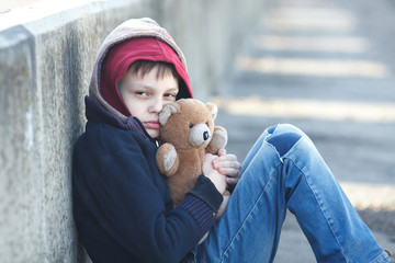 little homeless boy holding a teddy bear