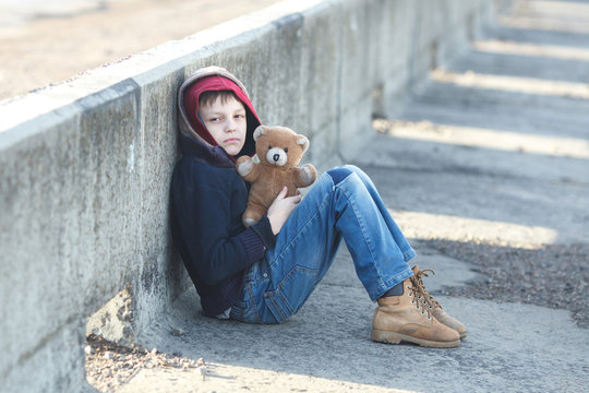 little homeless boy holding a teddy bear