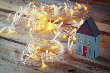 decorative house next to gold garland lights on wooden background. copy space
