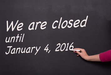 Fototapeta premium woman's hand with chalk on blackboard writing we are closed