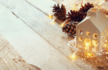 photo of pine cones and decorative wooden house next to gold garland lights on wooden background. copy space. retro filtered
