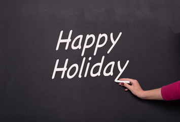 Fototapeta premium woman's hand with chalk on blackboard writing happy holiday