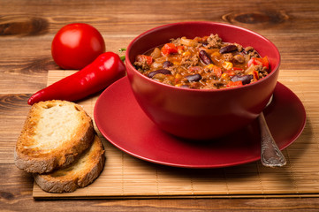 Chile con corne served in the red bowl on the wooden background.