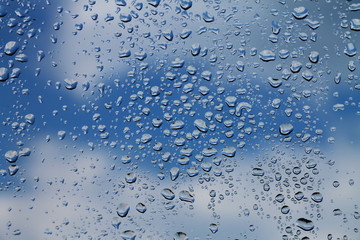 Rain drops on window with blue cloudy sky in background