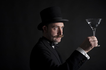 Man in top hat and examining a cocktail glass. It is a low key studio portrait
