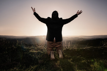 Man with outstretched arms
Rear view of a man with outstretched arms, kneeling in the grass on top of a hill.