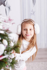 Obraz na płótnie Canvas Beautiful little girl in earmuffs decorating Christmas tree with