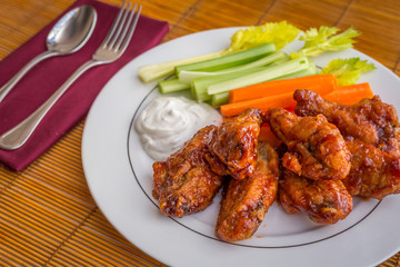 Tasty plate of glazed chicken wings with carrots, celery and dipping sauce.