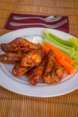 Tasty plate of glazed chicken wings with carrots, celery and dipping sauce.