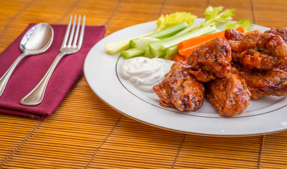 Tasty plate of glazed chicken wings with carrots, celery and dipping sauce.