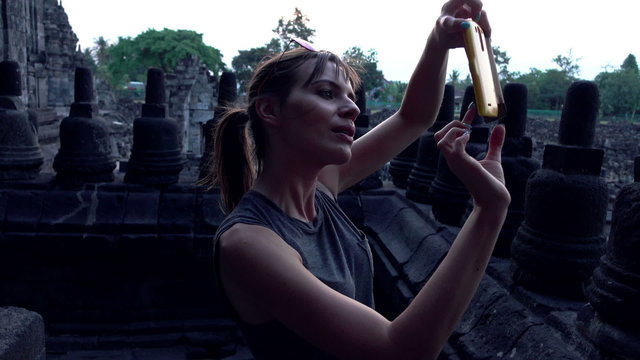 Young woman taking photos of Prambanan temple ruins in Indonesia
