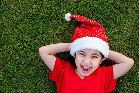 Little Asian Girl In Santa Hat On The Green Grass