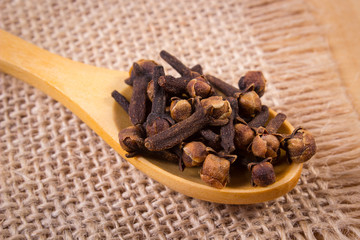 Heap of cloves with wooden spoon on jute canvas, seasoning for cooking