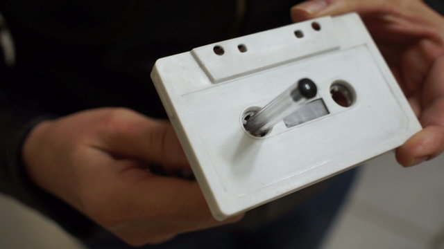Close up handheld shot of an anonymous in a black leather jacket slowly rewinding an eighties vintage or retro style magnetic tape audio cassette with a pen.