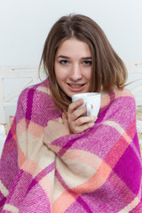 Sick woman covered with blanket holding cup of tea